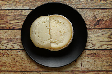 Torta del Casar cheese on a black plate on wooden table top view