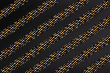Pattern of gold colored paper clips on a black paper background. Paperclip.