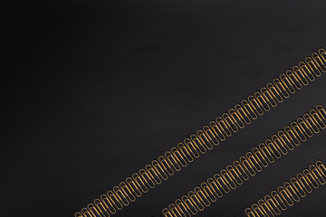 Pattern of gold colored paper clips on a black paper background. Paperclip.