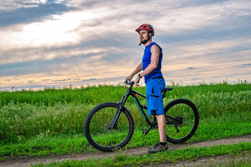 Fototapeta premium A young man in a helmet with a bicycle standing near the field.