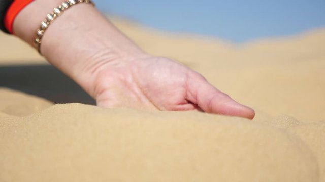 Young hand taking hot sand and sifting it down on a sunny day in desert in slo-mo