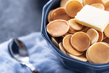 cereal pancakes in blue bowl with butter, spoon on blue gauze on grey background