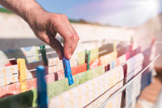 Male hands hanging up colorful clothes or kitchen towels on the clothesline with clothespins on the terrace on a sunny day. Equitable distribution of household chores. Homework. Do laundry.