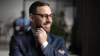 Smiling businessman wearing glasses dreaming about good future close up, touching chin, business...