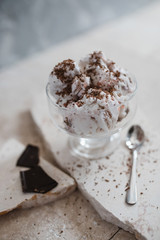 Vanilla ice cream sprinkled with chocolate chips in a transparent bowl on a light stone background