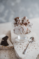 Vanilla ice cream sprinkled with chocolate chips in a transparent bowl on a light stone background