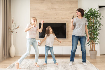 Happy mother and two daughters having fun singing karaoke song in hairbrushes. mother laughing...