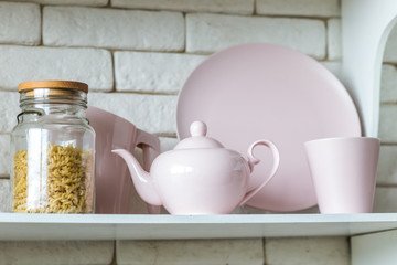 
Glass jar with vermicelli on a shelf next to a pink teapot and a pink plate.