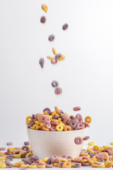 Colorful cereal rings flowing into the white bowl isolated on white background.