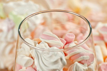 Sweets in a glass on a wooden table. Transparent utensils with marshmallows and biz. Pink with white soft candies close up.