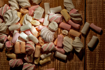 Lots of sweets on a wooden table. Pink with orange marshmallows and bize close up. Candy on a shabby old board.