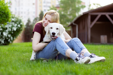 girl with a puppy of a retriever sits on a green grass in the spring on the street, a woman plays...