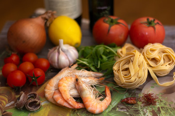 Ingredients for fettuccine with shrimps: white wine, olive oil, saffron, arugula, chilli, anchovies, garlic, cherry tomatoes, lemon, onion, toamto, shrimps and fettuccine.