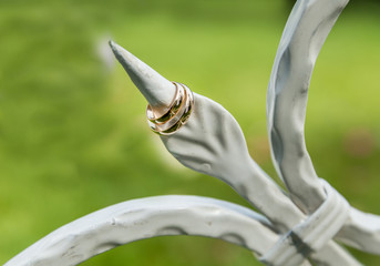 
Wedding rings close-up are photographed on a vintage white stand on a sunny summer day with a green background.