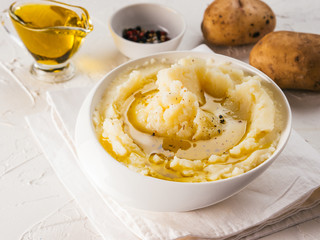 Mashed potatoes in white bowl with cloth napkin, pepper and olive oil on textured concrete white background