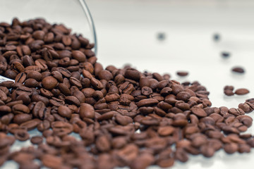 Coffee beans pour out of a glass bowl onto a light surface. coffee background, close-up, selective focus