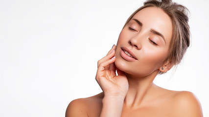 Close up of a brunette cute woman face with fresh clean flawless skin. She touches her face with her hand. Studio beauty portrait on white background