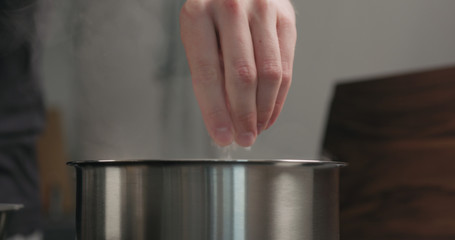 man hand salting boiling water in saucepan