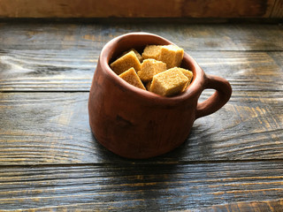 pieces of brown sugar in a ceramic mug on a wooden background