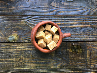 pieces of brown sugar in a ceramic mug on a wooden background