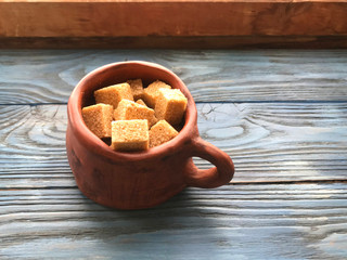 pieces of brown sugar in a ceramic mug on a wooden background