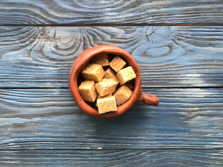 pieces of brown sugar in a ceramic mug on a wooden background
