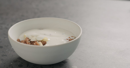 yogurt over chocolate granola in white bowl on terrazzo surface