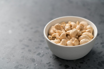 Dry cashew nuts in white bowl on concrete background with copy space