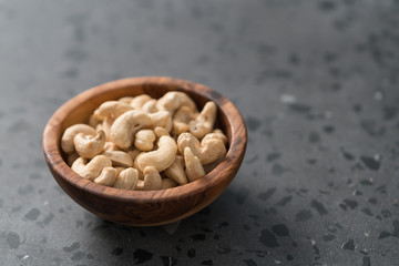 Dry cashew nuts in wood olive bowl on concrete background with copy space