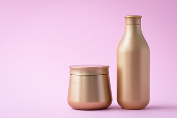 Golden flacon of shampoo and a jar of mask. Cosmetic products on a pink background. Luxury beauty style, hair care concept. Clear bottles. Copy space, empty place for text.