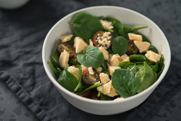 Salad with spinach, kumato tomatoes and cheese in white bowl on linen napkin