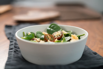 Salad with spinach, kumato tomatoes and cheese in white bowl on linen napkin