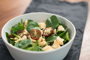 Salad with spinach, kumato tomatoes and cheese in white bowl on linen napkin