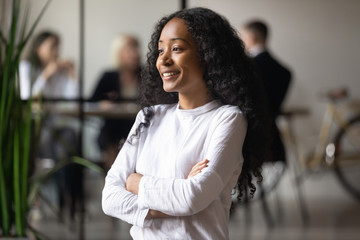 Head shot smiling African American businesswoman dreaming about good future, business vision concept, female team leader boss standing in modern office, looking in distance, thinking about project