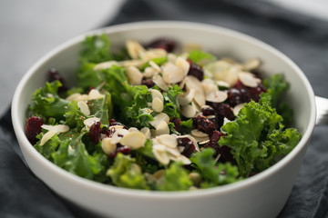 Salad with kale, cranberries and almond flakes in white bowl on linen napkin