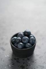 Fresh ripe blueberries in small black bowl on concrete background with copy space