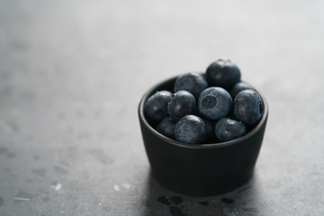 Fresh ripe blueberries in small black bowl on concrete background with copy space