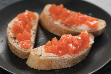 Bruschettas with salmon and cream cheese on black plate closeup