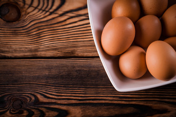 Detail close-up of chicken eggs on the old brown wooden background.
