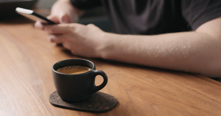 unrecognizable man sitting at the walnut table with smartphone and drink fresh espresso