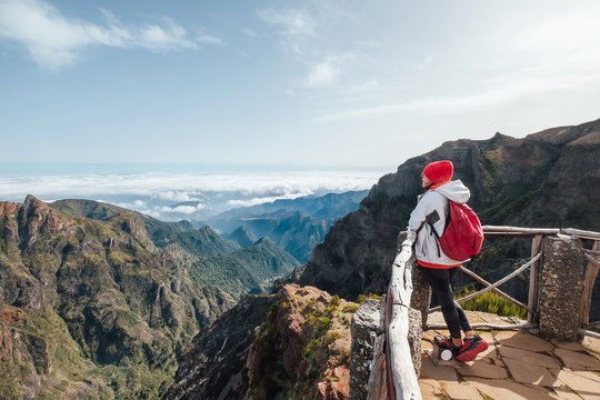 Young female backpacker enjoying mountains view while trekking by famous mountain footpath from Pico do Arieiro to Pico Ruivo on the Portuguese Madeira island. Around the world traveling concept image