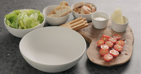 Man hand add romaine lettuce and dressing to make caesar salad in white ceramic bowl on concrete countertop