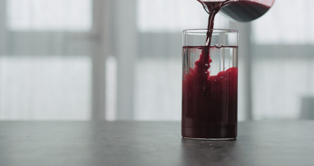 pour blueberry juice in water in beaker glass on concrete countertop with window on a background