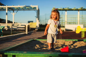 Happy baby child playing with the sand at the playground at sunset.
