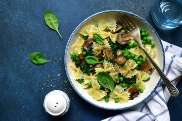 Pasta farfalle with mushrooms, spinach and green pea. Top view with copy space.