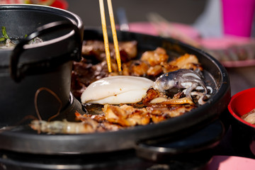 Grilled meat on pan and people use chopsticks for eating 