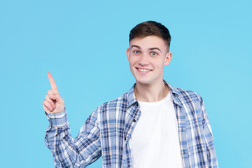 Cheerful smiling guy dressed in white t-shirt, checkered shirt on blue background. Young man is showing with fingers number one, percents, discount. Male gesturing. Emotional portrait concept.