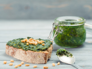 Close up view of whole grain rye bread with fresh basil pesto sauce on gray wooden table. Copy space.