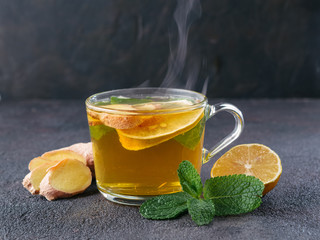 Herbal tea with ginger, mint and lemon. Hot tea glass cup with steam and ingredients on black...