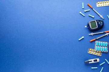 Digital glucometer, lancet pen, tablets, syringes on blue background with space for text, flat lay....